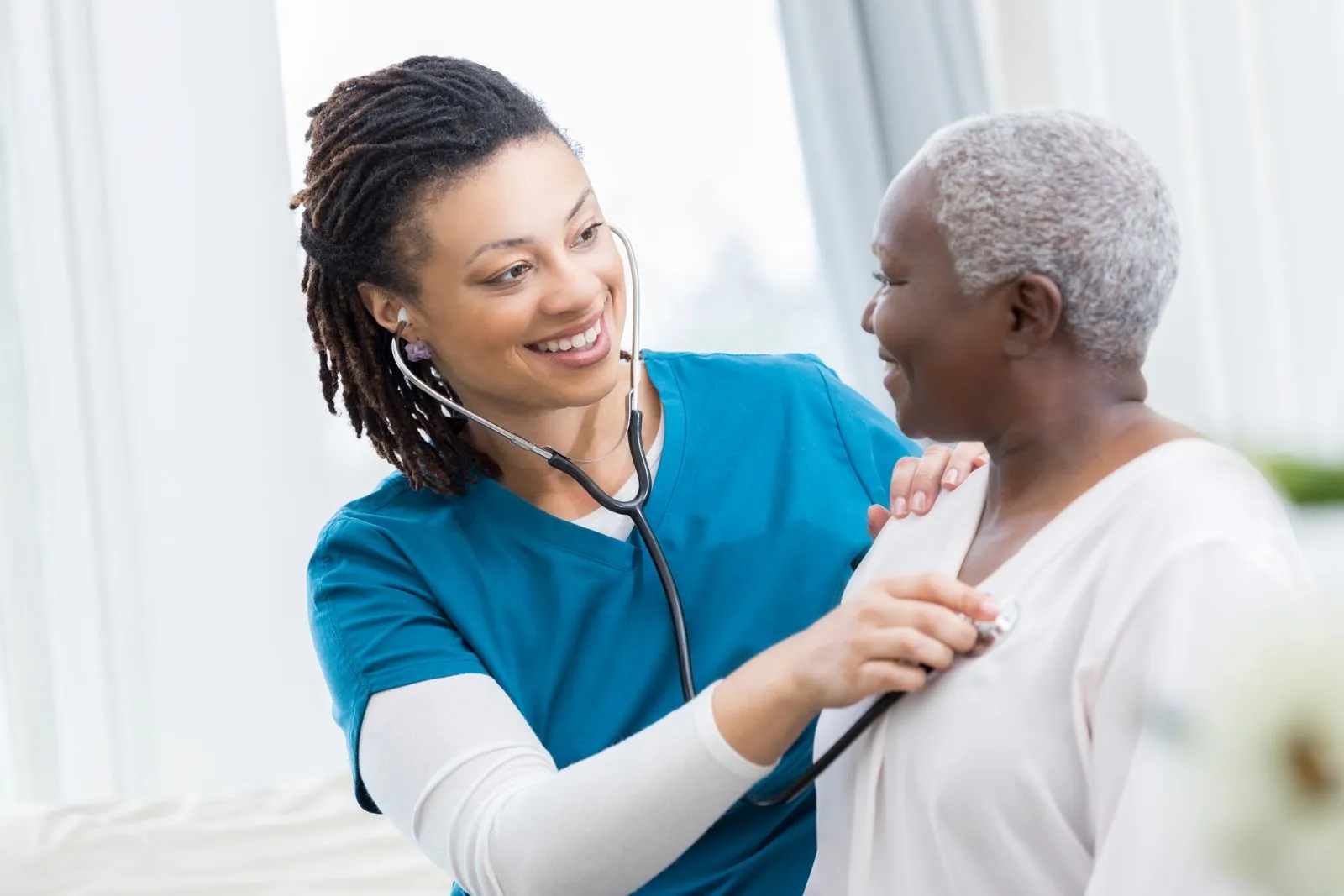 A caregiver with her hand on the shoulder of a smiling older woman